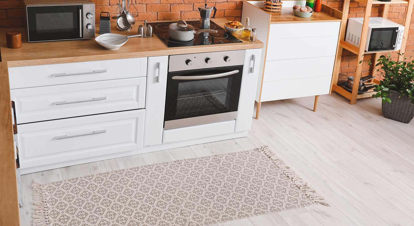 Tiny kitchen with white cabinets, wood countertops, and gray and cream patterned rug.