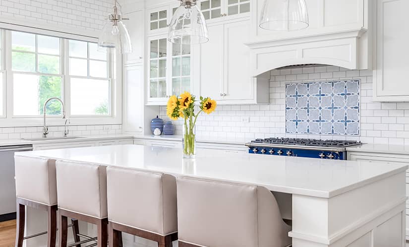 Transitional kitchen with white backsplash and patterned blue tiles above range.