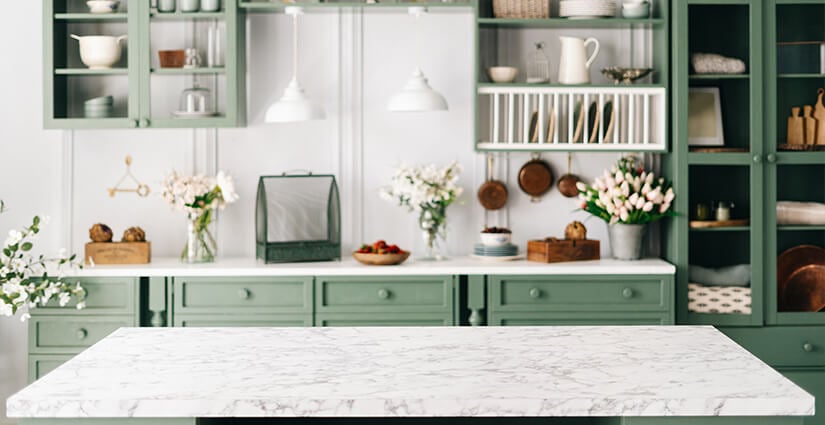 Kitchen with green cabinets and large island with white and gray travertine countertop.