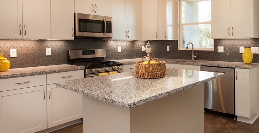 Kitchen with white countertops, brown tiled backsplash and brown, white and black speckled granite countertop.
