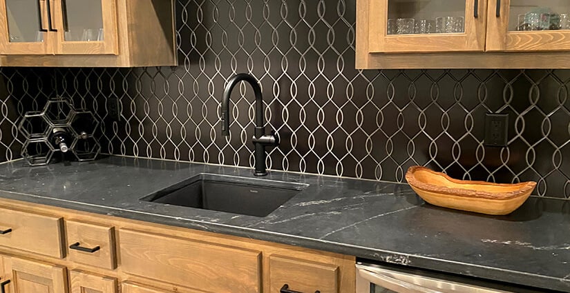 Kitchen with wood cabinets, black geometric backsplash and black soapstone countertops with white veining.