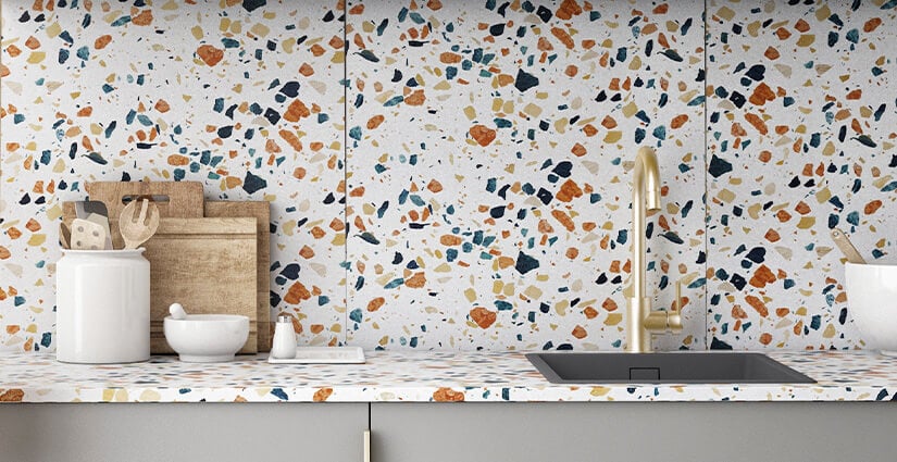 Close up of colorful terrazzo kitchen countertop and backsplash with gold sink.