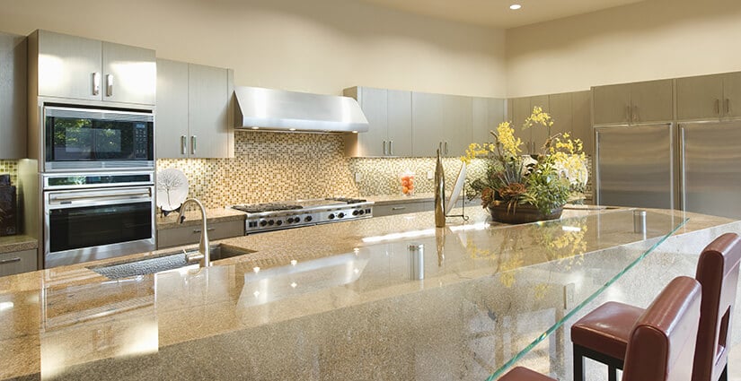 Large kitchen with gray cabinets and beige kitchen island with abstract glass countertop.