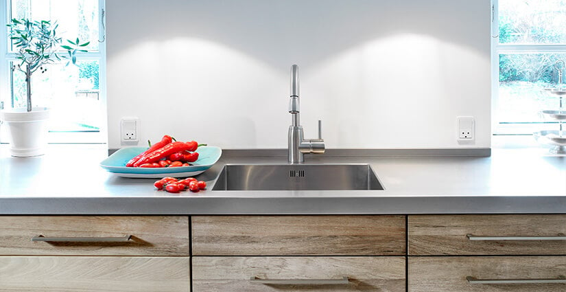 Kitchen with sink integrated into stainless steel countertop with blue plate of red peppers on top.